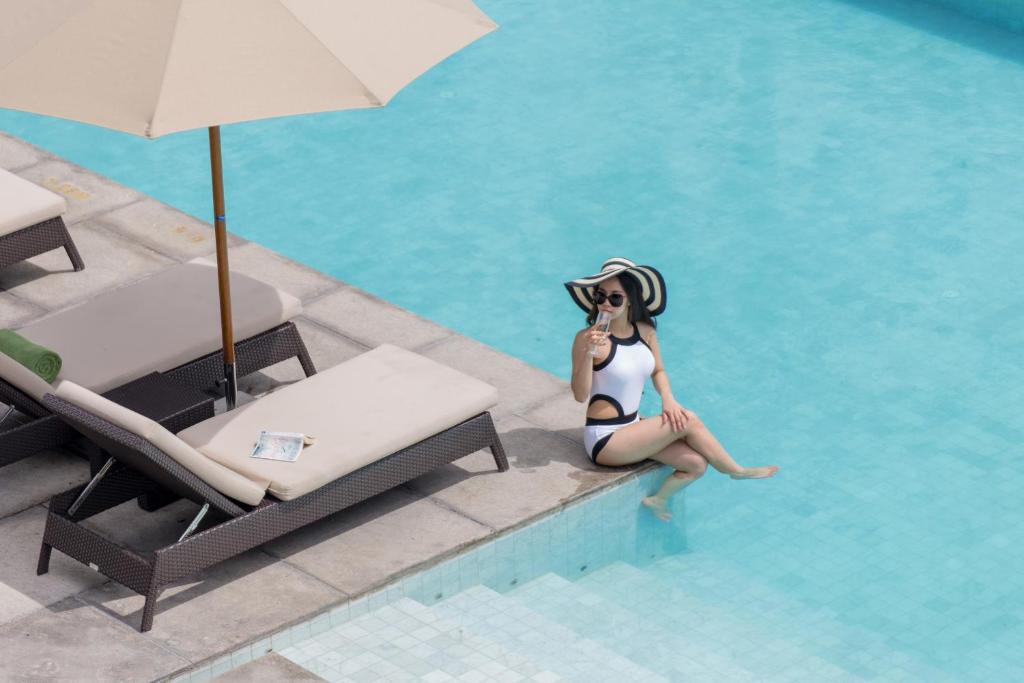 A guest sits at the pool edge beside loungers and a large umbrella.