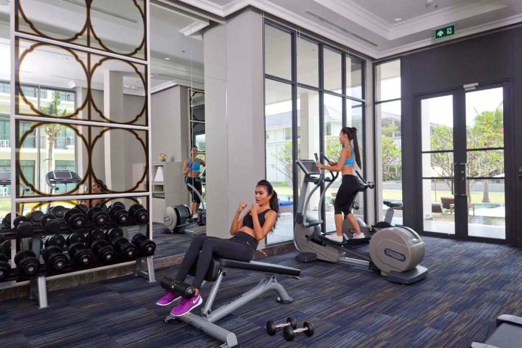 A sunlit gym with treadmills, an elliptical, dumbbells and an adjustable bench.
