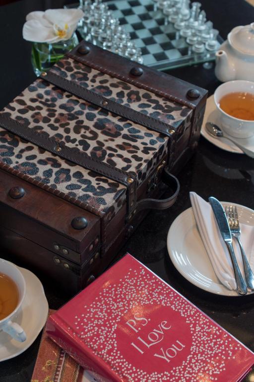 A tea setting with a leopard-print suitcase, chessboard, crockery and a red book.