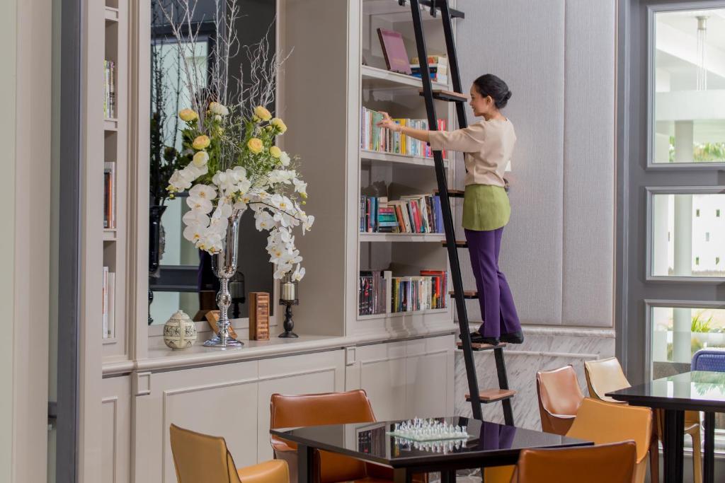 A library-lined lounge or dining area combines a rolling ladder, floral display, and dark tables.