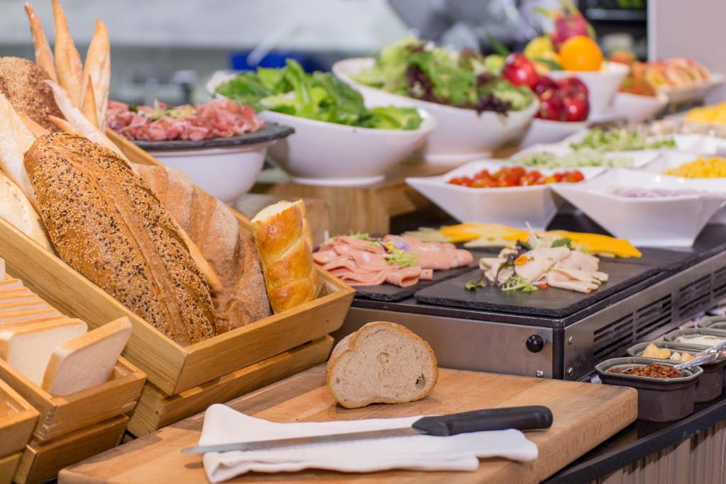 A breakfast buffet presents sliced breads, cold cuts, salads, vegetables, and condiments.
