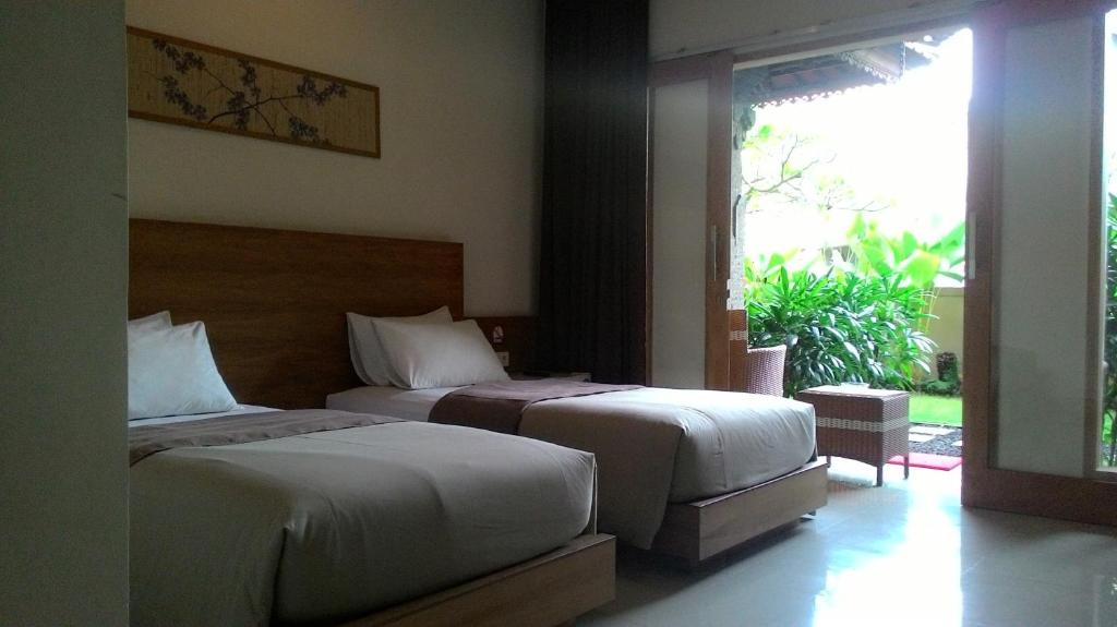 a bedroom with two beds and a large window at Kubu Carik in Legian