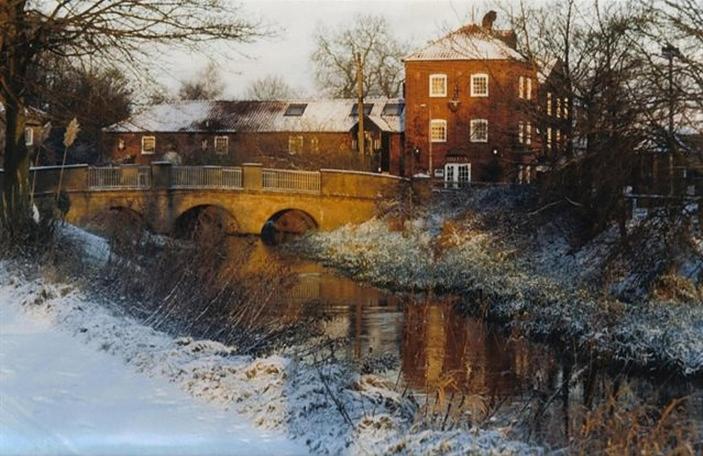 un puente sobre un río con un edificio al fondo en Wensum Lodge Hotel, en Fakenham