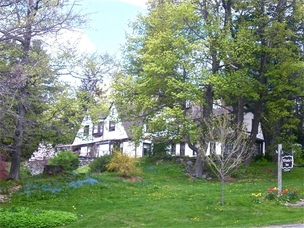a white house on a hill with trees at Whistler's Inn in Lenox