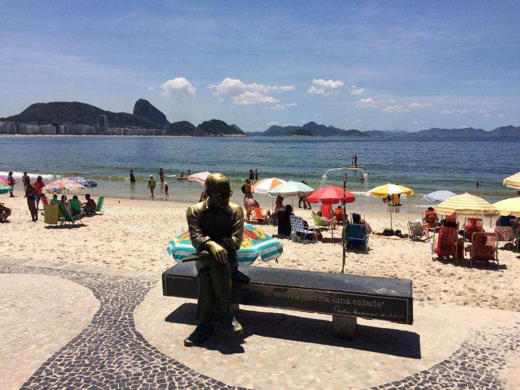 una estatua de un hombre sentado en un banco en una playa en COPACABANA 2 Quartos e Sala - QUADRA DA PRAIA no POSTO 6, en Río de Janeiro