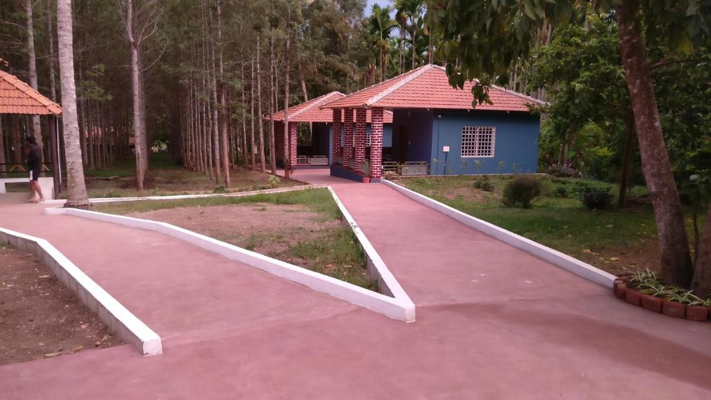 a walkway in front of a blue building with trees at The Shades Holiday inn in Kushālnagar