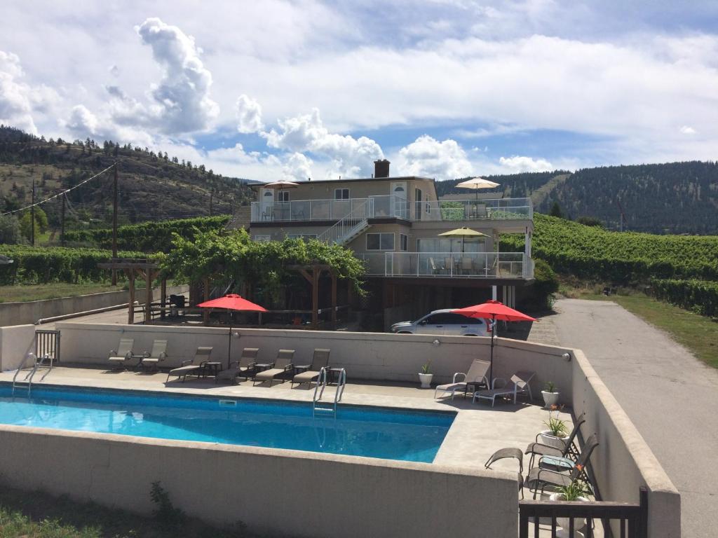 a pool with chairs and umbrellas next to a house at D'Angelo Winery Farm House in Penticton