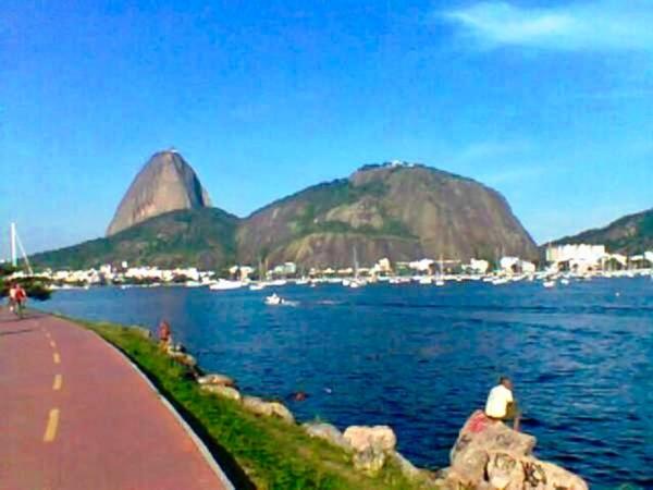 a person sitting on a sidewalk next to a body of water at Aragão Botafogo Studio in Rio de Janeiro