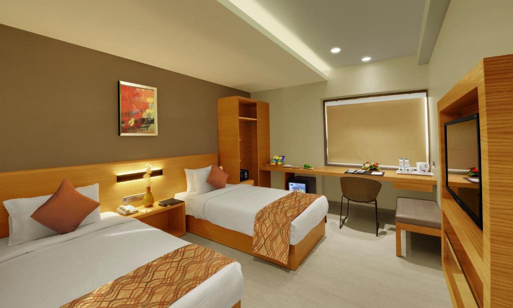 a hotel room with two beds and a desk at Hotel Suba Elite Vadodara in Vadodara