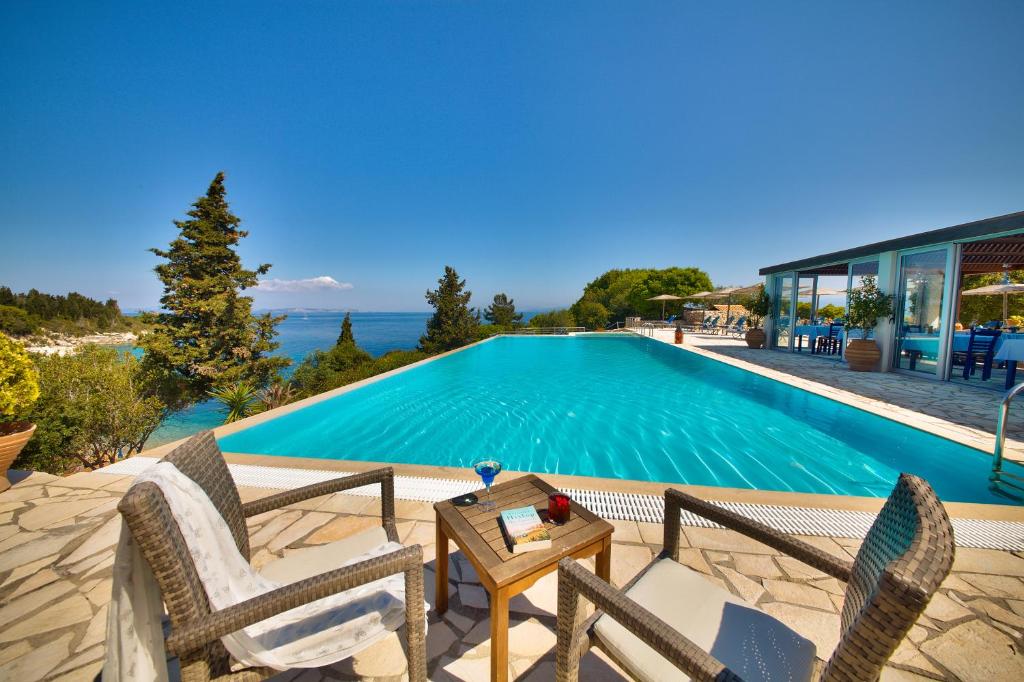 a villa with a swimming pool with two chairs and a table at Glyfada Beach Villas in Longos