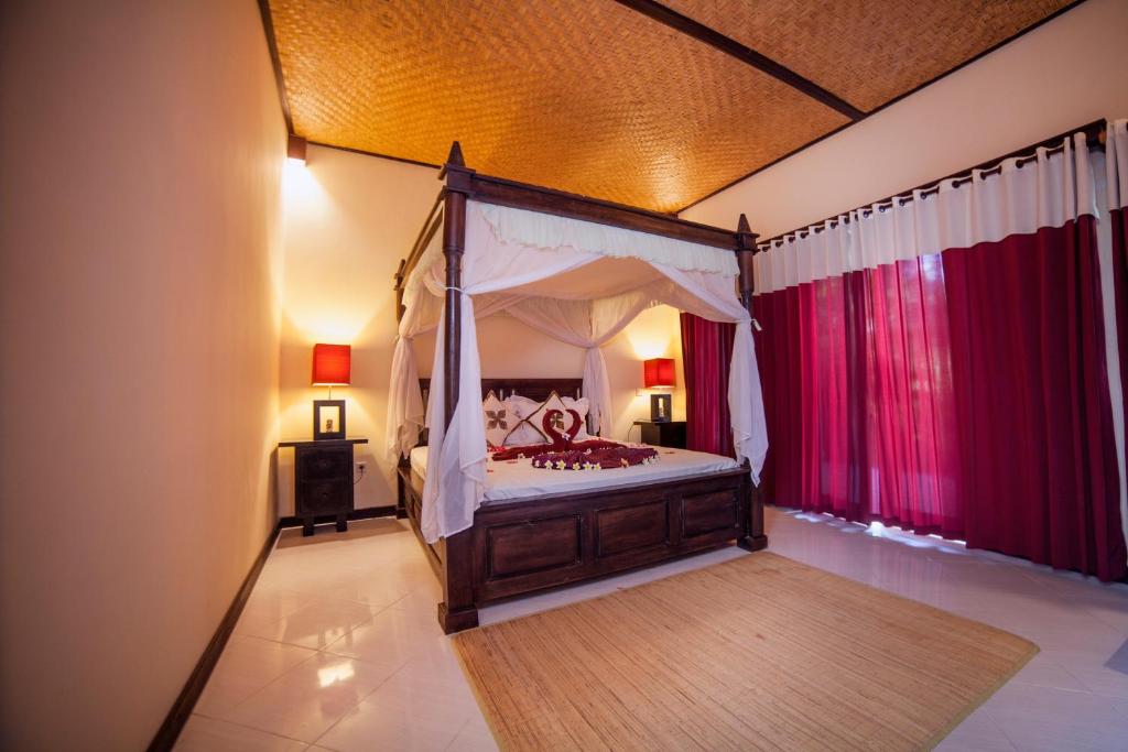 um quarto com uma cama de dossel e cortinas vermelhas em Mans Cottages & Spa em Pemuteran