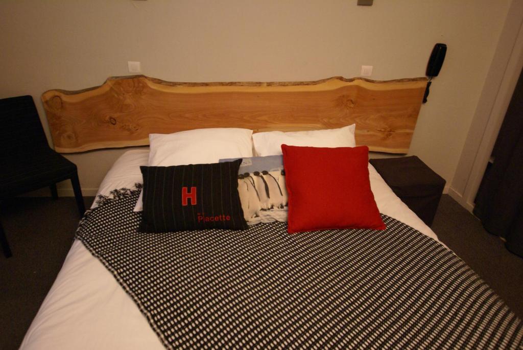 a bed with two red pillows on top of it at Hotel de la Placette Barcelonnette in Barcelonnette