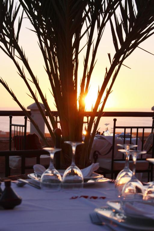 a table with plates and a vase with the sunset in the background at Hotel De Charme Les 3 Chameaux 4 étoiles in Mirleft