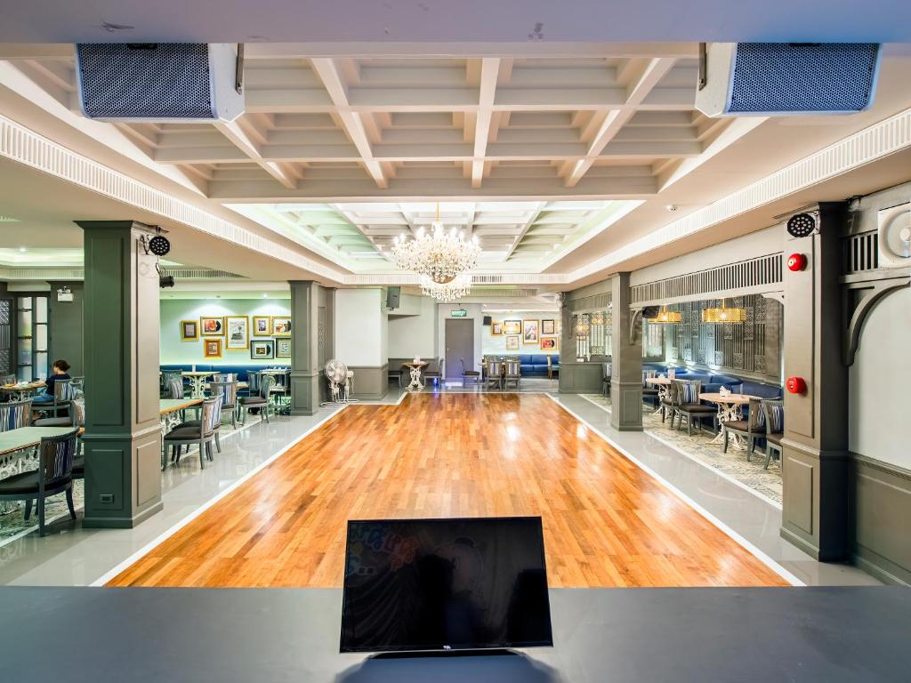 A grand hotel lobby with polished wooden flooring, chandelier lighting, and dining-style seating along both sides.