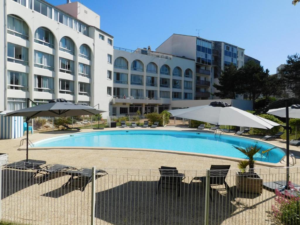 una piscina con sillas y sombrillas frente a un edificio en Résidence New Rochelle, en La Rochelle