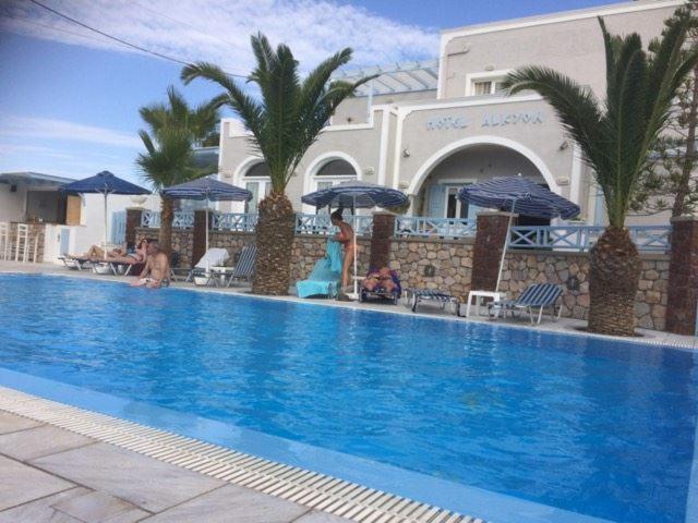 einen Swimmingpool mit Leuten, die unter Sonnenschirmen neben einem Gebäude sitzen in der Unterkunft Alkyon Hotel in Kamari