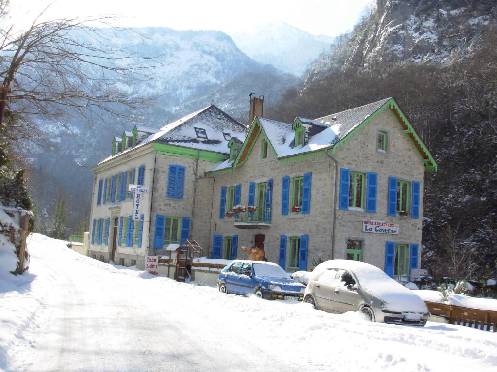 uma casa com janelas azuis e carros estacionados na neve em Auberge La Caverne em Laruns