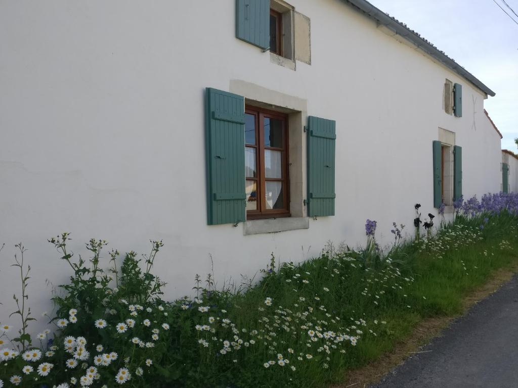 a white house with green windows and flowers at Des Km à La Ronde in La Ronde