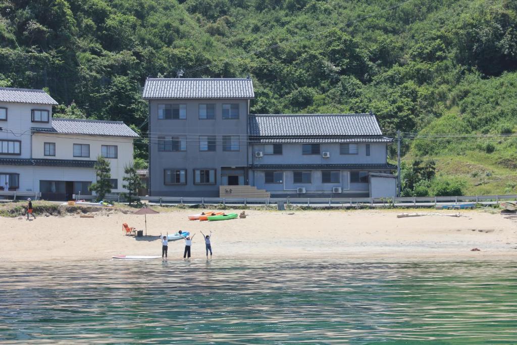 un grupo de personas de pie en una playa con casas en Uminone, en Toyooka