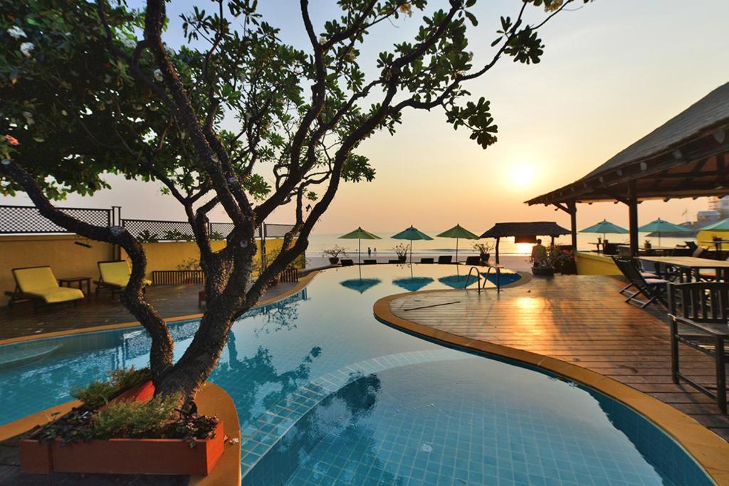 a swimming pool with a tree in the sunset at Supatra Hua Hin Resort in Hua Hin