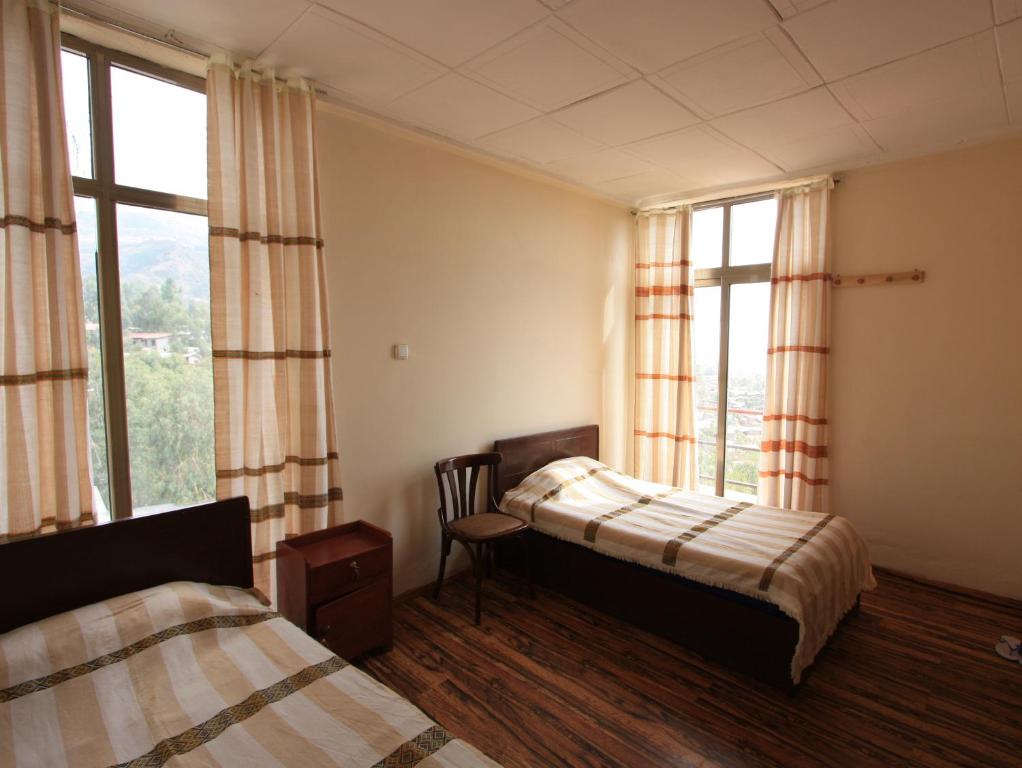 a bedroom with two beds and a chair and windows at Red Rock Lalibela Hotel in Lalībela