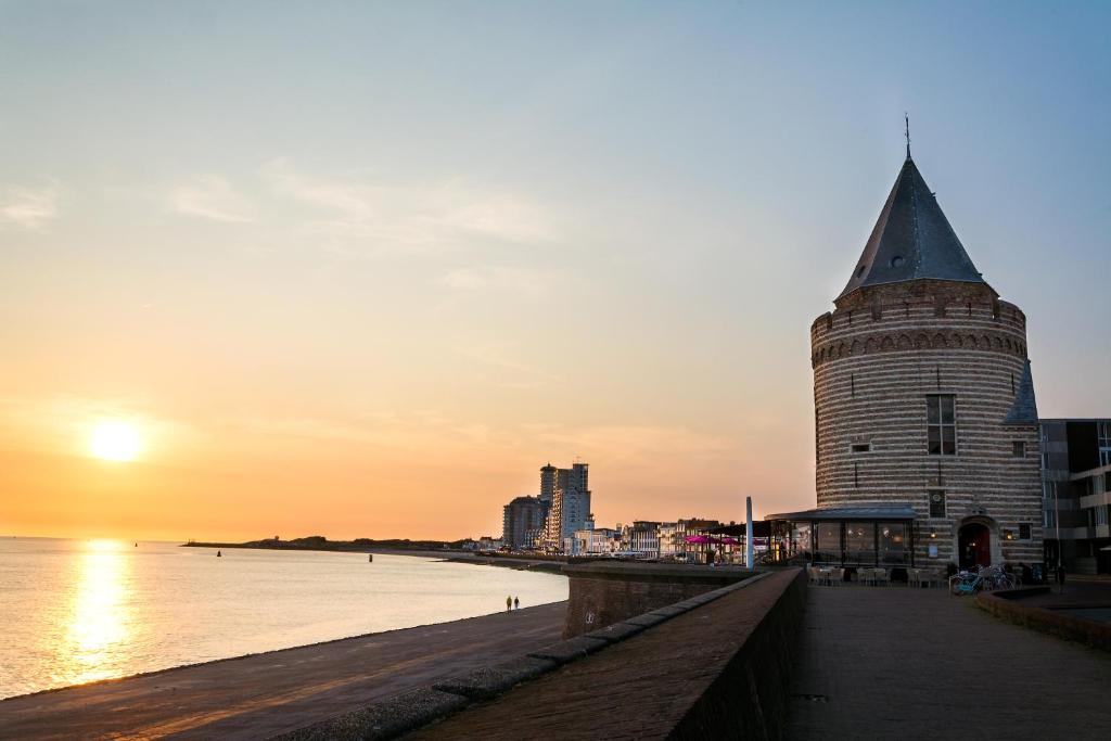 a building on the beach with the sunset in the background at De Gevangentoren Suite in Vlissingen