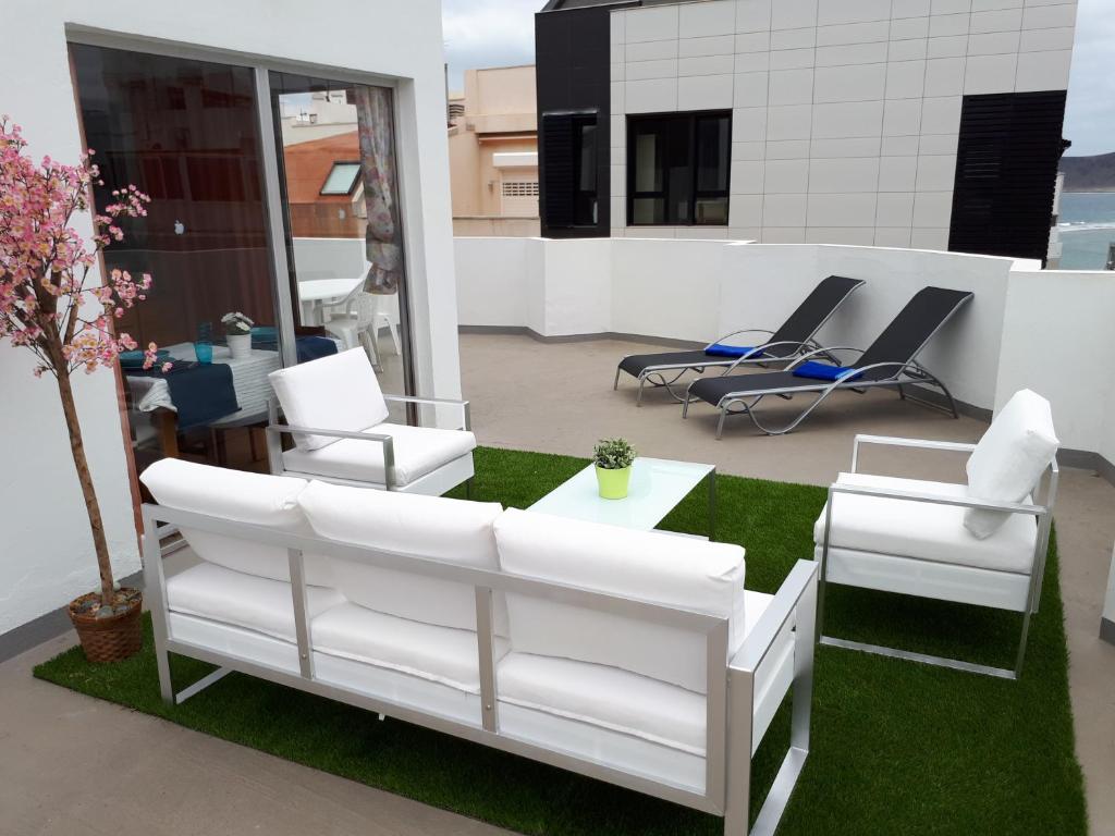 un patio con sillas blancas, mesa y césped en City Beach Home 60, en Las Palmas de Gran Canaria