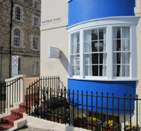 a blue and white building with a window and a fence at Valentine Guest House in Weymouth