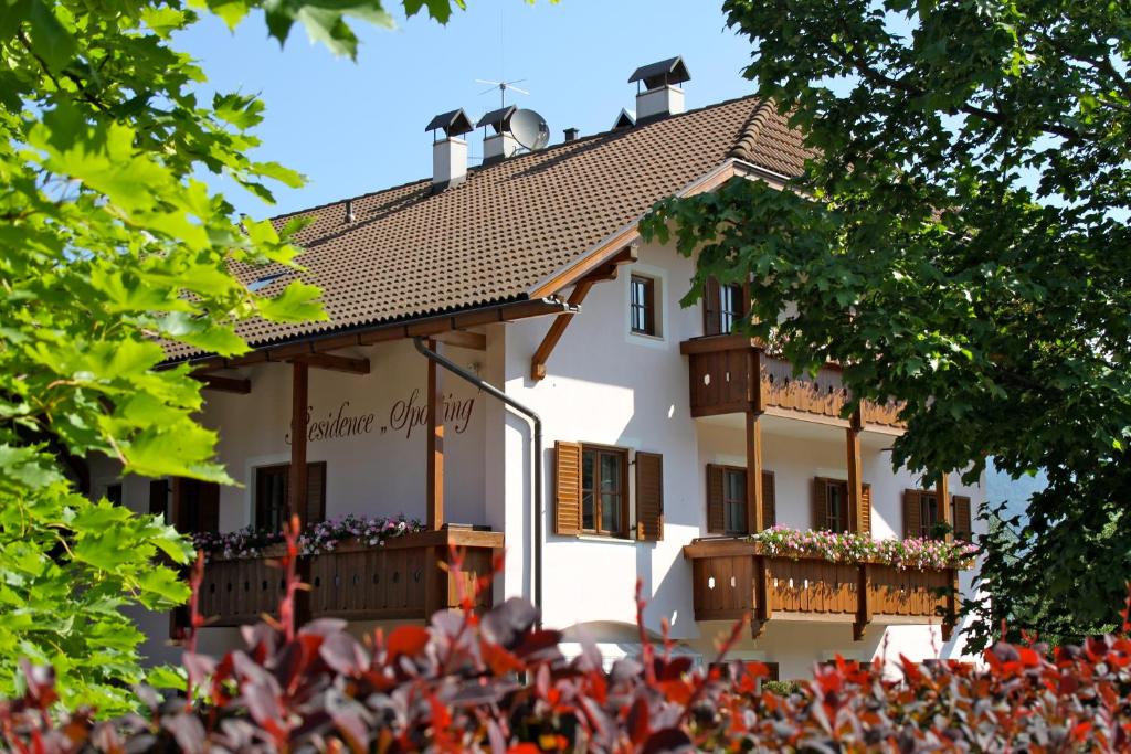 a white house with wooden balconies and trees at Residence Sporting in Brunico