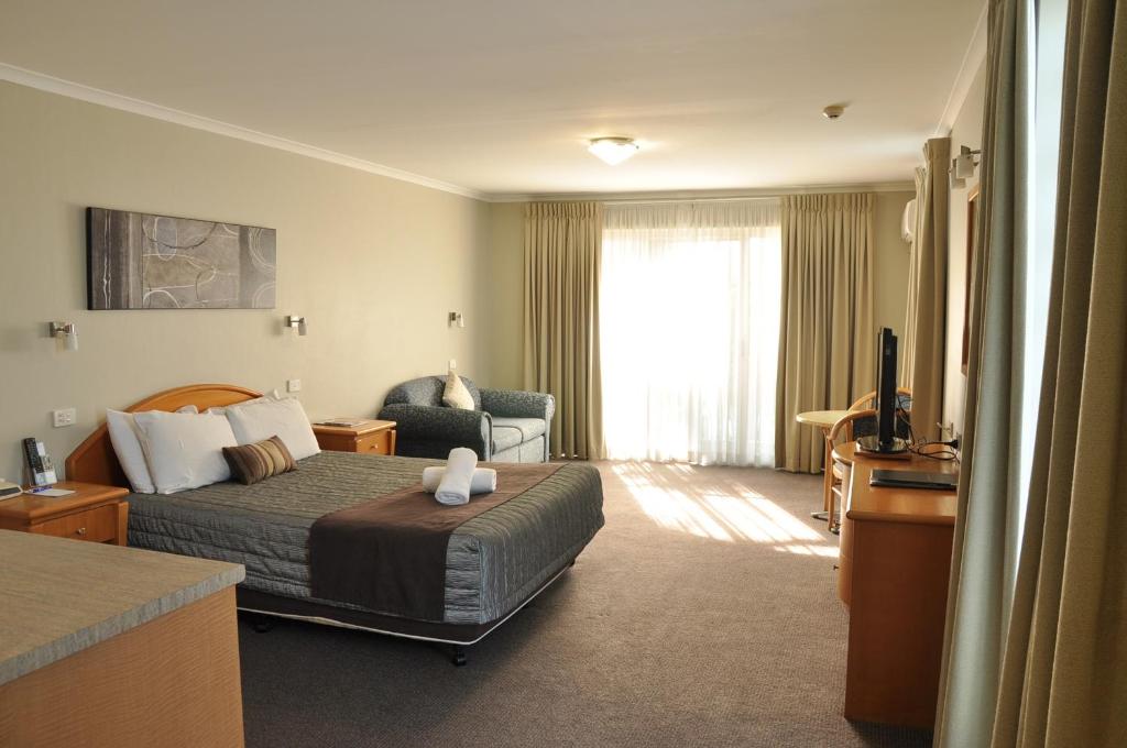 a bedroom with a bed, chair and a lamp at Chittaway Motel in Tuggerah