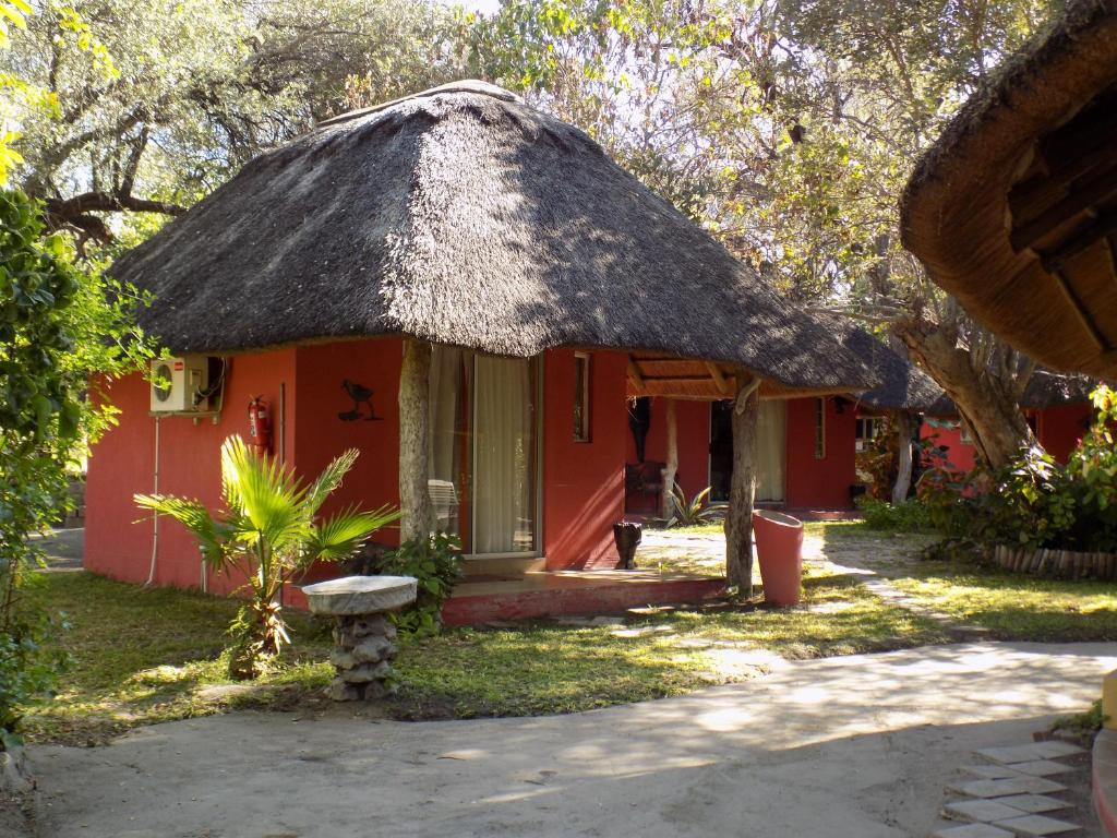 a small red house with a thatched roof at Jump Street Chalets in Maun