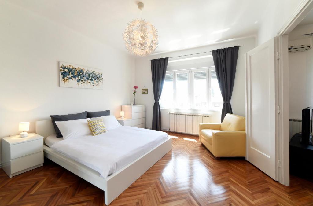 a white bedroom with a bed and a chair at Apartment Sunny, Zagreb City Center in Zagreb