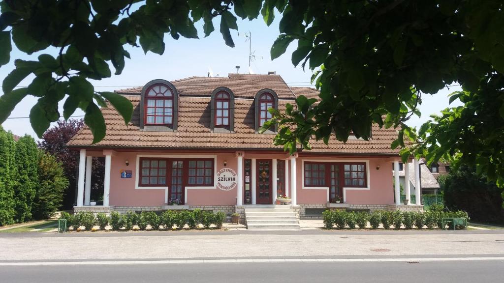 ein rosafarbenes Haus mit braunem Dach in der Unterkunft Szilvia Gästehaus in Bük