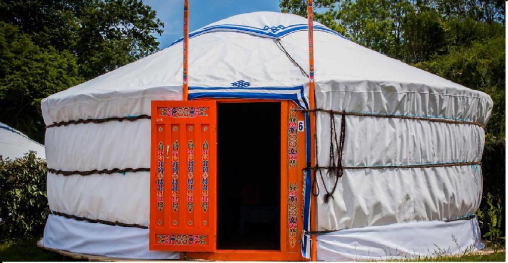 a yurt with an orange door in the middle at Le Village Insolite yourte et roulotte in Saint-Benoît-des-Ondes
