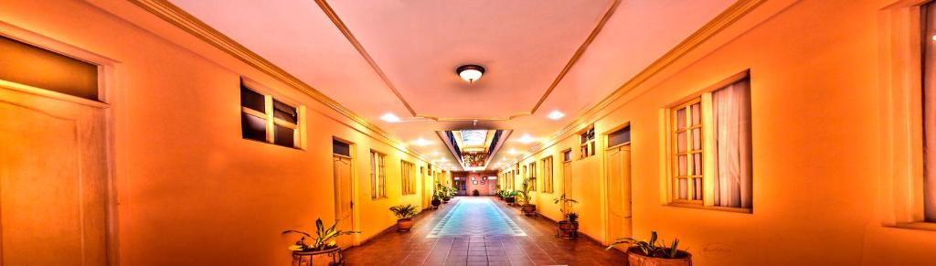 a hallway with orange walls and a long hallway with plants at Hotel Monserrat in Cochabamba