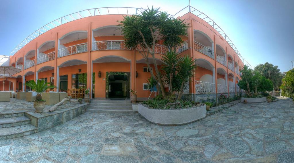 an orange building with palm trees in front of it at Hotel Benitses Arches in Benitses