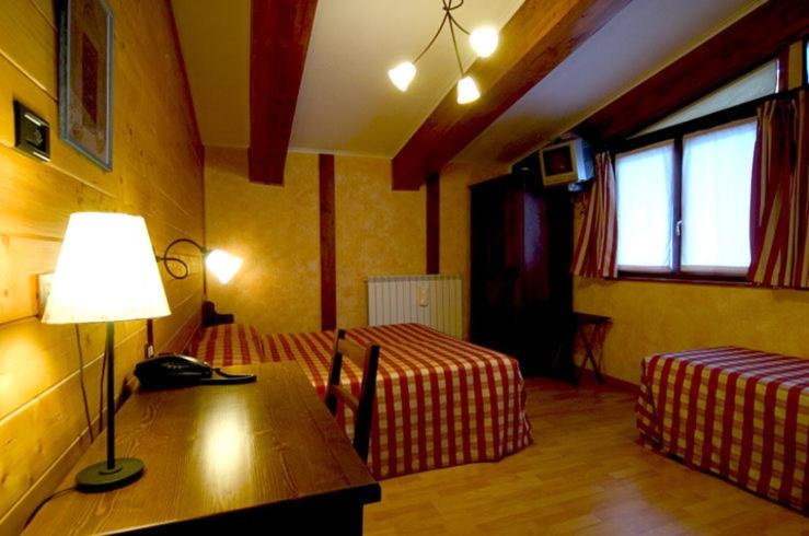a room with two beds and a table with a lamp at Hotel La Pigna in Bardonecchia