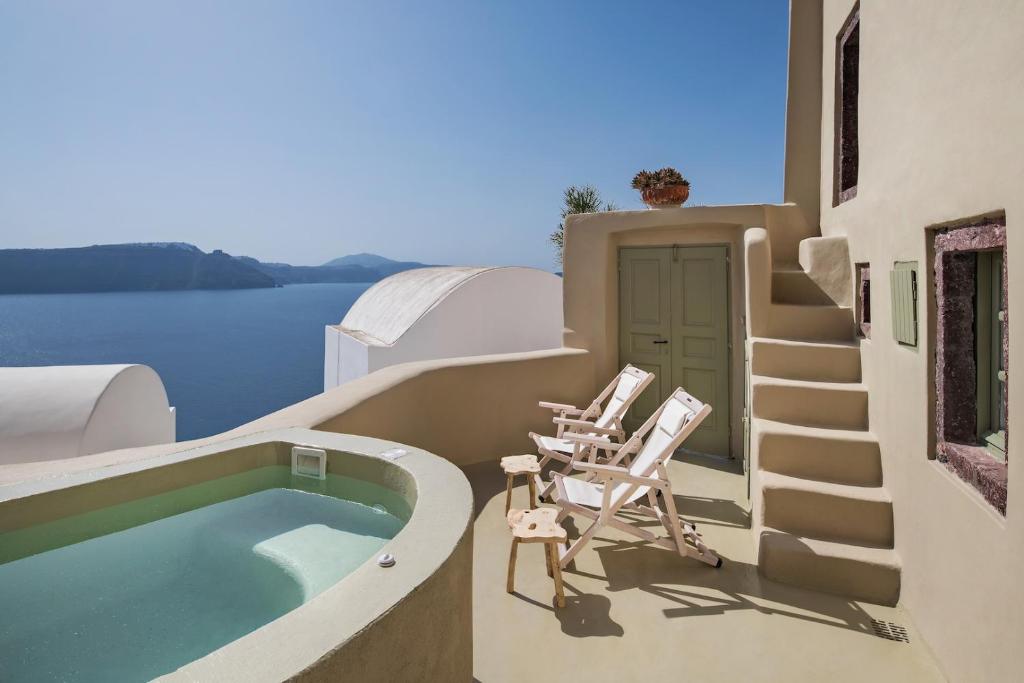 a balcony with two chairs and a swimming pool at Cosmoia Cave House in Oia