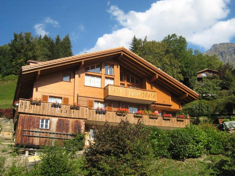 a large wooden house with a balcony on a hill at Chalet Protea in Wengen