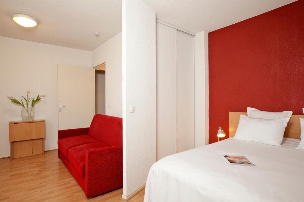a bedroom with a bed and a red chair at Séjours & Affaires Paris-Nanterre in Nanterre