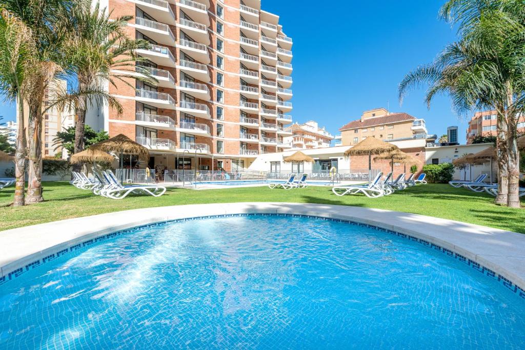 a swimming pool in front of a building with palm trees at Hotel Mainare Playa in Fuengirola