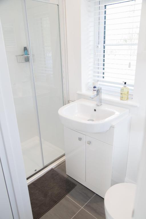 a white bathroom with a sink and a shower at Linden House in West Wittering
