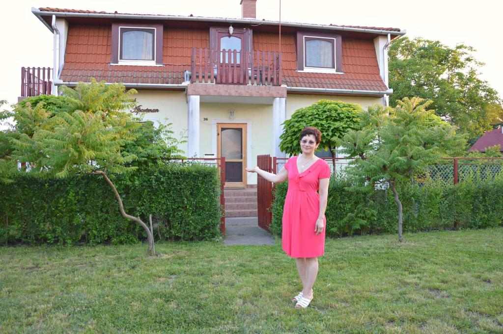 Una mujer con un vestido rojo parada frente a una casa en Florianus Vendeghaz, en Berekfürdő