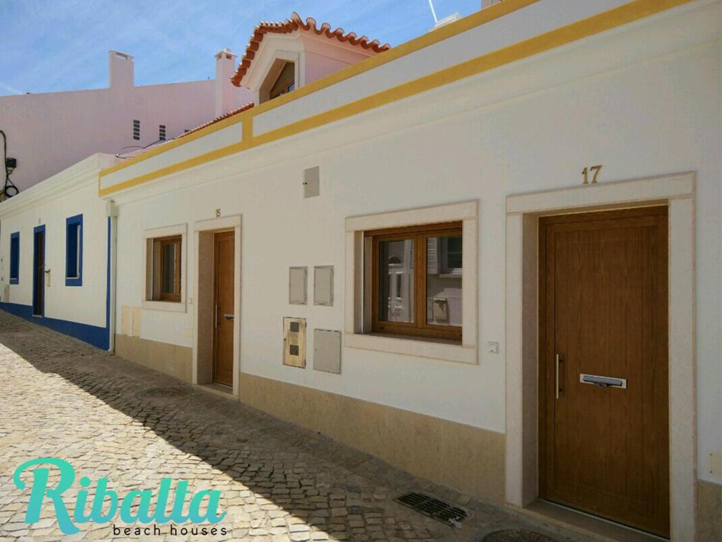 a white building with brown doors on a street at Ribalta Beach Houses in Ericeira