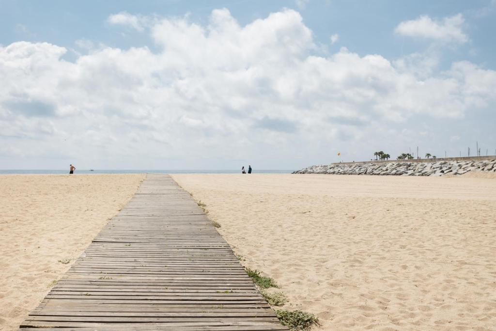 un camino de madera en una playa de arena con gente a lo lejos en Vilasardemarlux1, en Vilassar de Mar