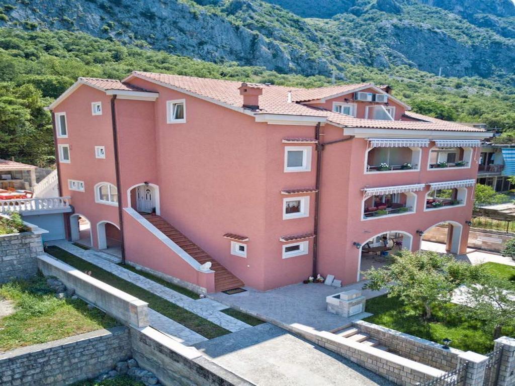 un grand bâtiment rose avec des montagnes en arrière-plan dans l'établissement Apartments Radonjić, à Kotor