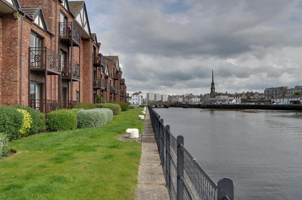 a river with buildings and a fence next to the water at Harbour House - Donnini Apartments in Ayr