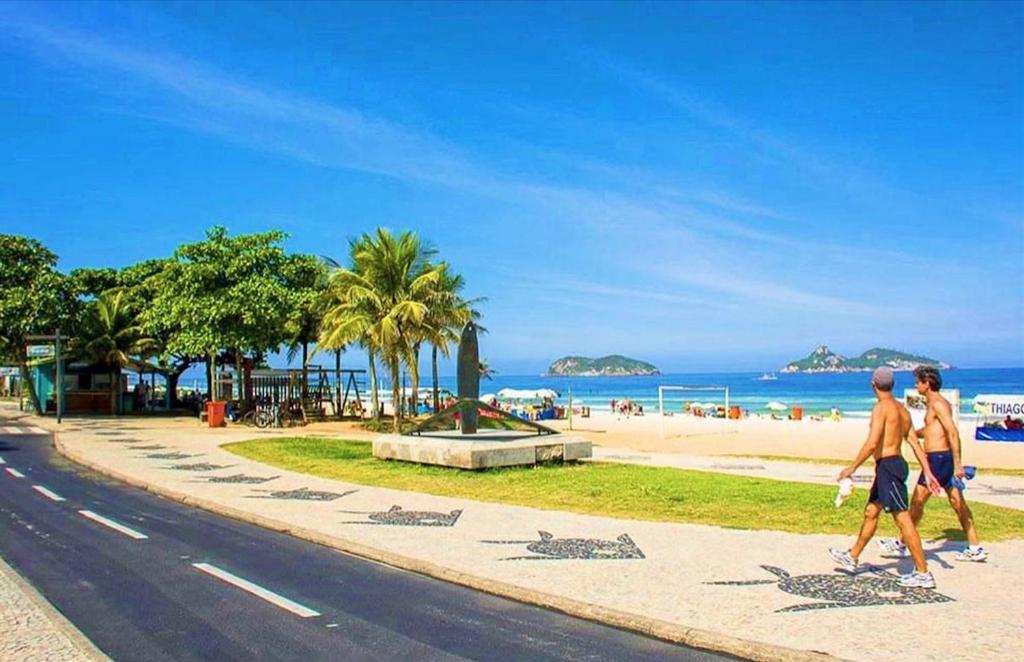 two men walking down a sidewalk next to the beach at Beach Guest House - Go Make A Trip in Rio de Janeiro