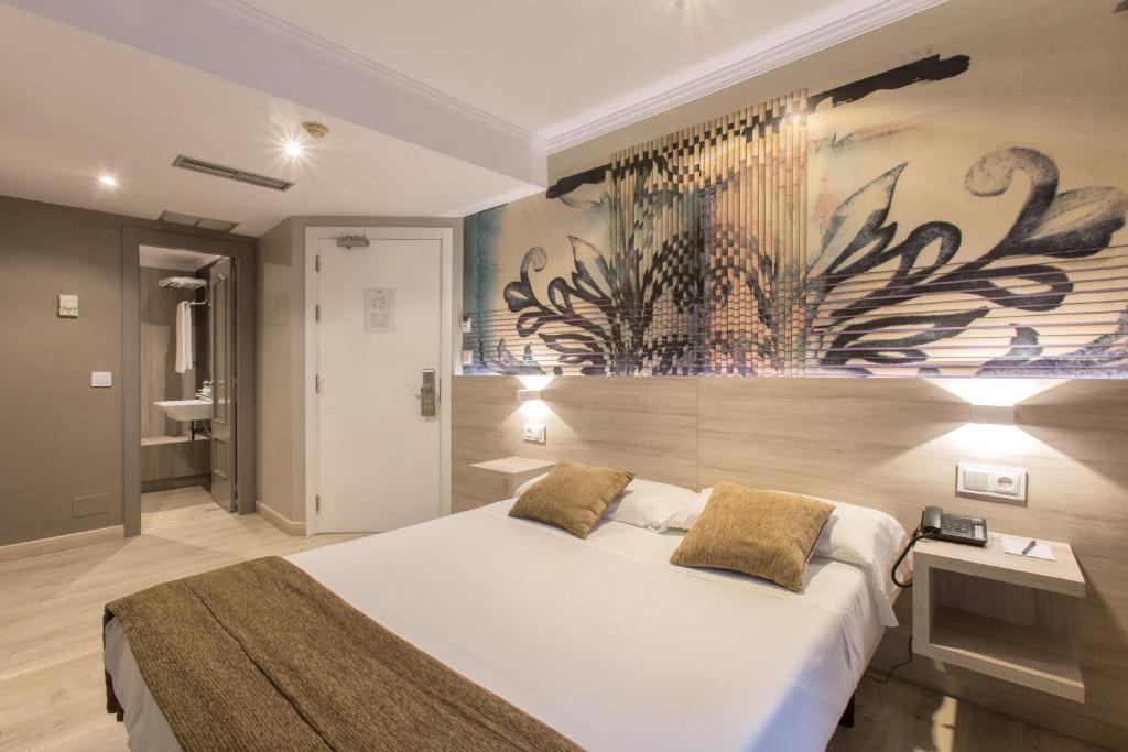 サンティアゴ・デ・コンポステーラにあるHotel Alda San Carlosの大きなベッド付きのベッドルーム1室、壁に絵画が飾られています。
