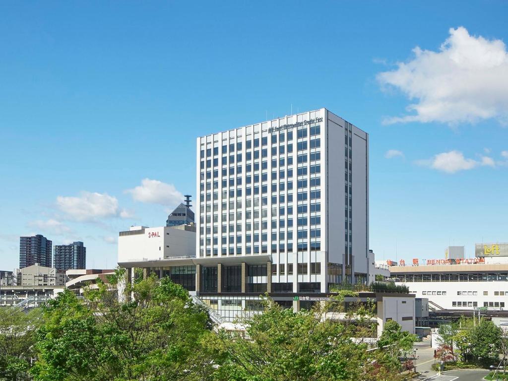 un edificio alto y blanco con árboles delante en Hotel Metropolitan Sendai East en Sendai